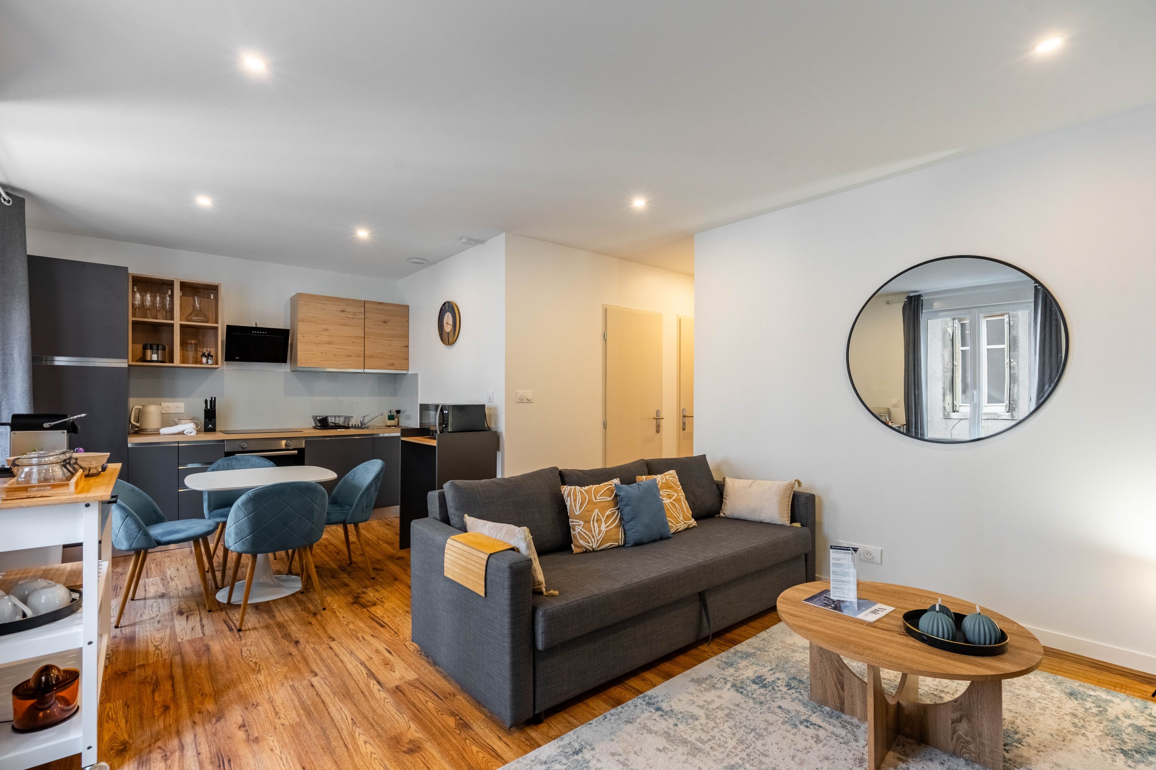A modern living area with a sofa, chairs, a coffee table, and a kitchen in the background.