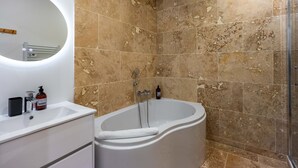 Een badkamer met een vrijstaand bad, een ronde spiegel en een witte wastafel met lades.