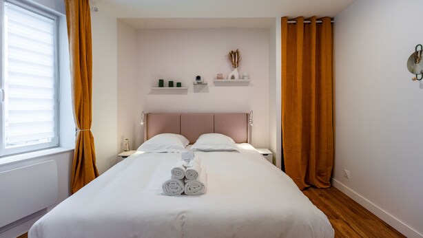 Een net opgemaakt bed met opgerolde handdoeken, een hoofdeinde, nachtkastjes en planken met decoratieve objecten.