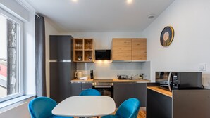 Een compacte keuken met moderne apparaten, een eethoek met blauwe stoelen en een raam dat natuurlijk licht binnenlaat.