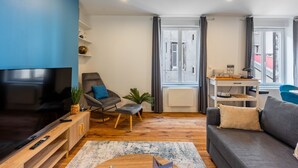 Een moderne woonkamer met een flatscreen televisie, een grijze bank, een houten tv-meubel en een groot raam met gordijnen.