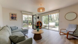 A modern living room with a sofa, a round wooden coffee table, a chair, and large windows. - So Dune - La Teste 5km de la Plage (La Teste-de-Buch)