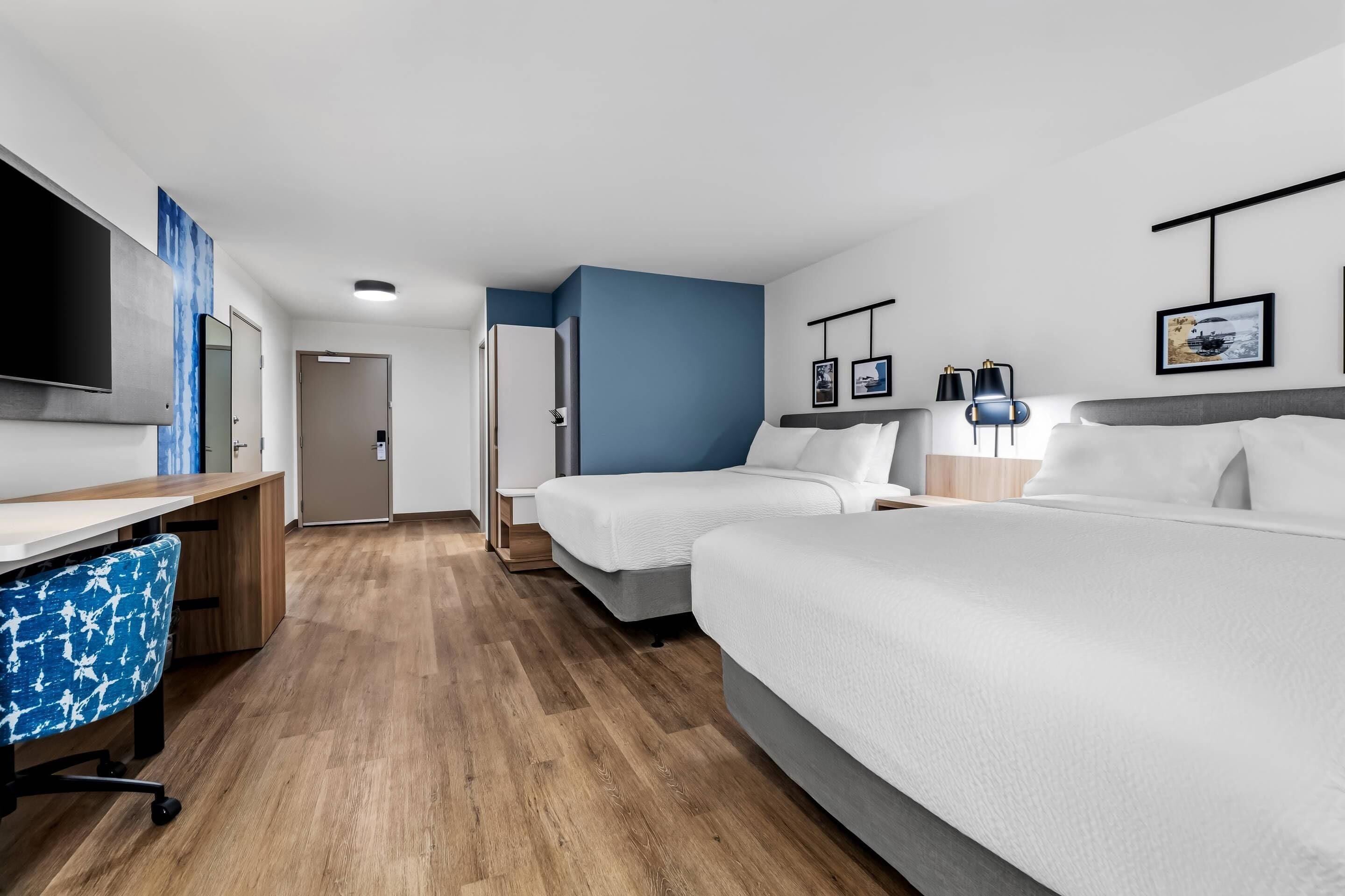 Een hotelkamer met twee bedden, een bureau, een stoel, een televisie en een deur.