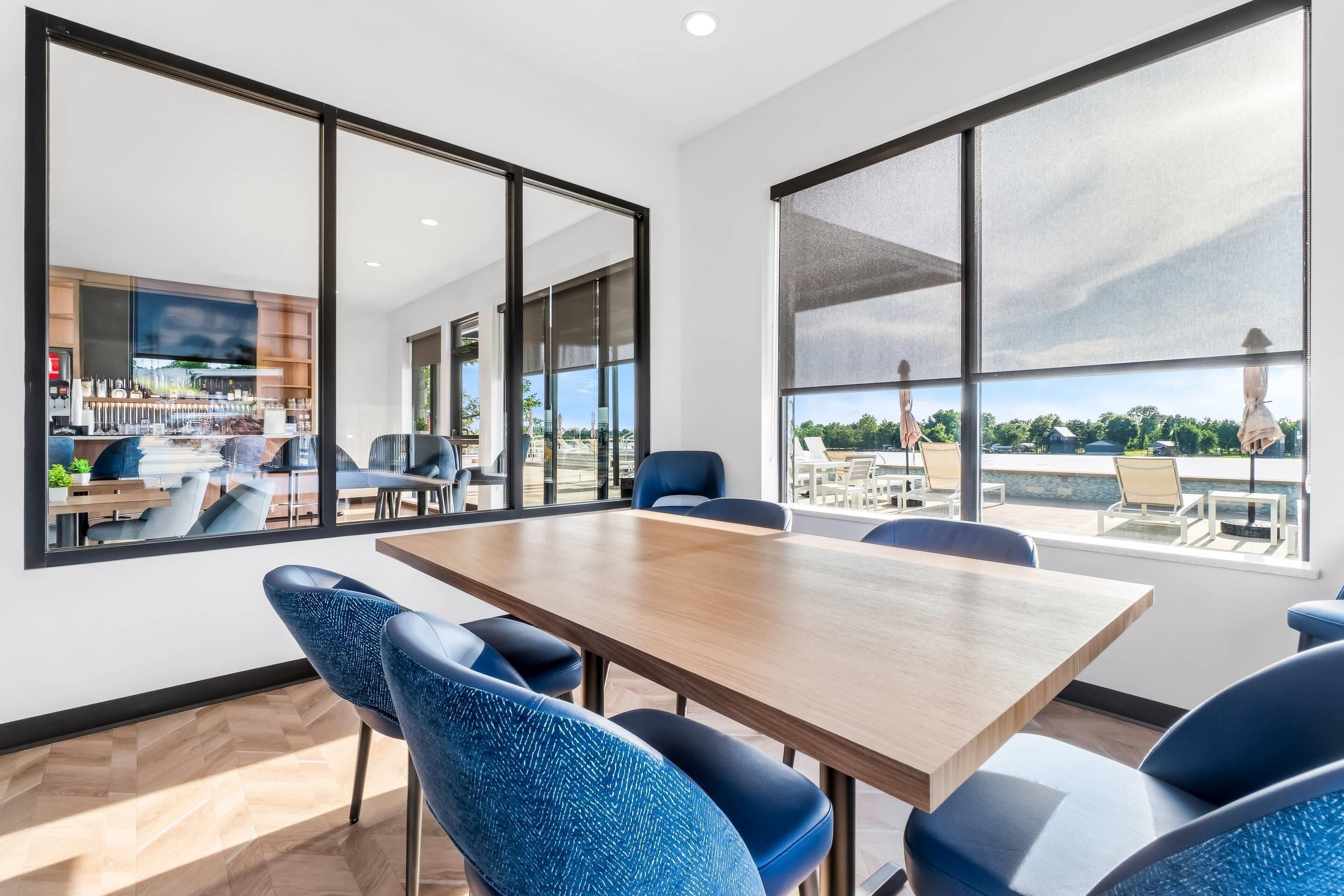 A modern conference room with a large table and chairs, large windows, and a view of outdoor seating.