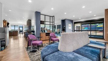 A modern hotel lobby with a seating area, a reception desk, and large windows offering a view of the outside.