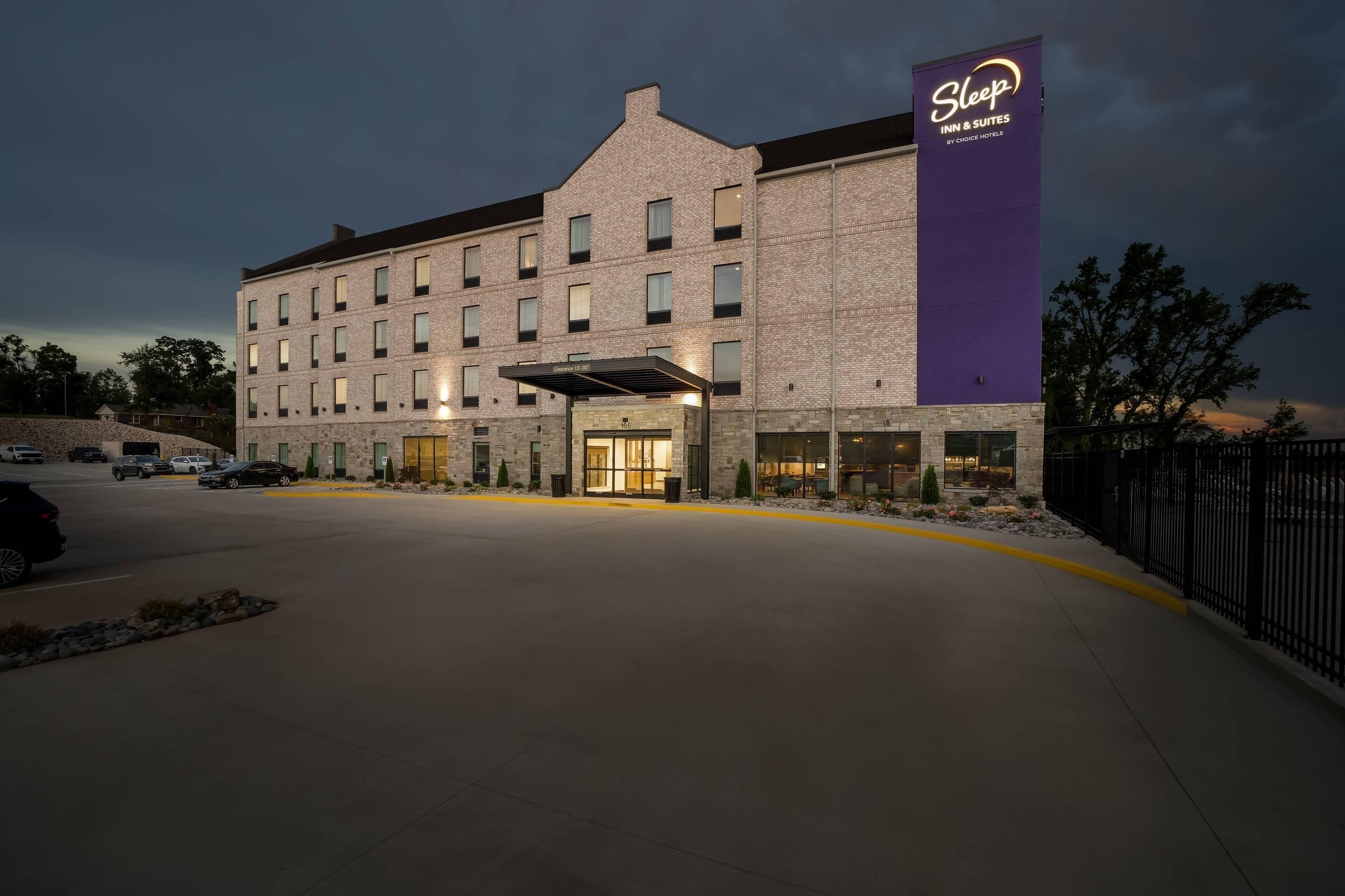 Un hotel con fachada de ladrillo, un llamativo letrero de Sleep Inn & Suites y una entrada cubierta.