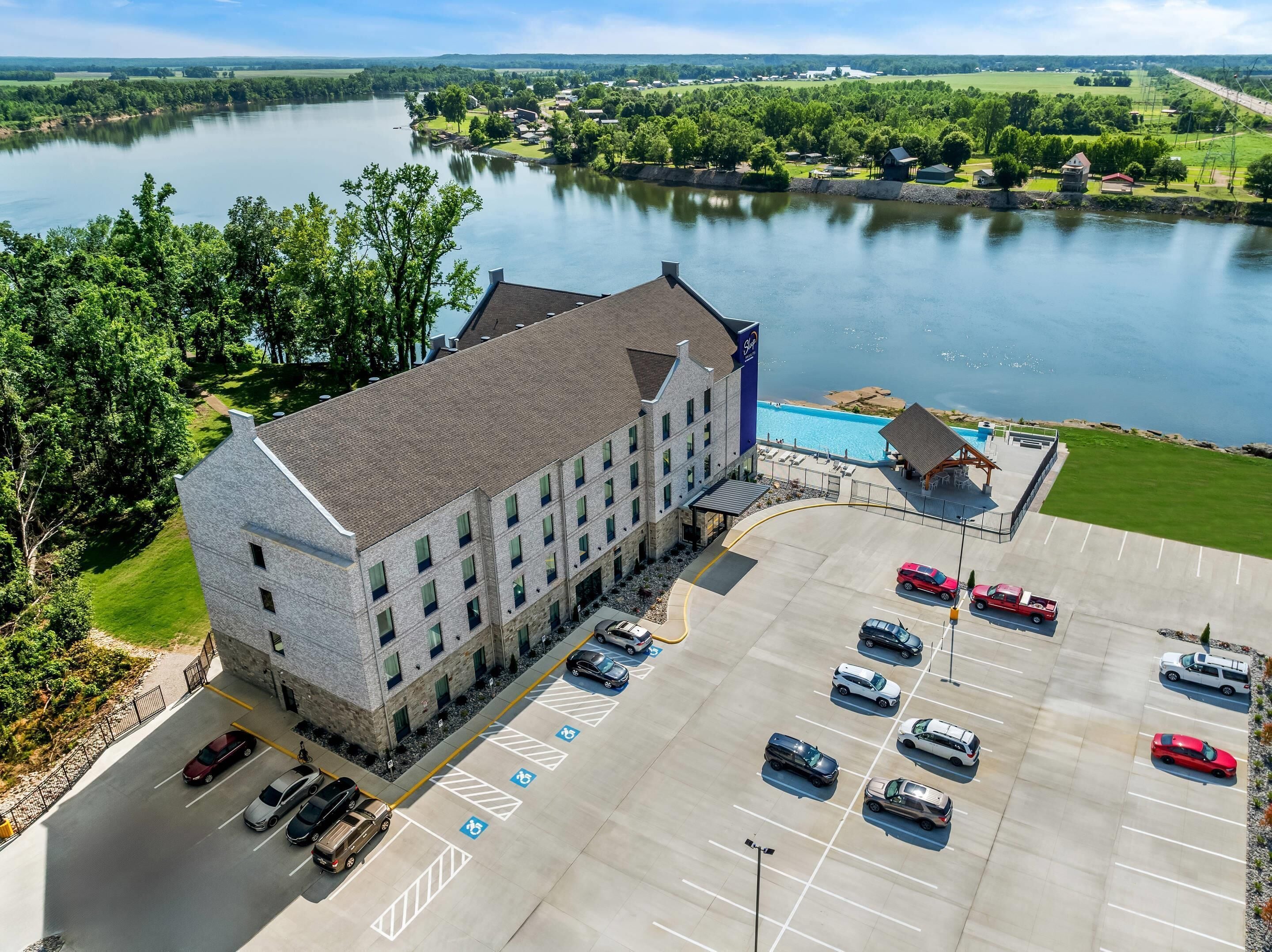 A hotel with a parking lot, a swimming pool, and a view of a lake.