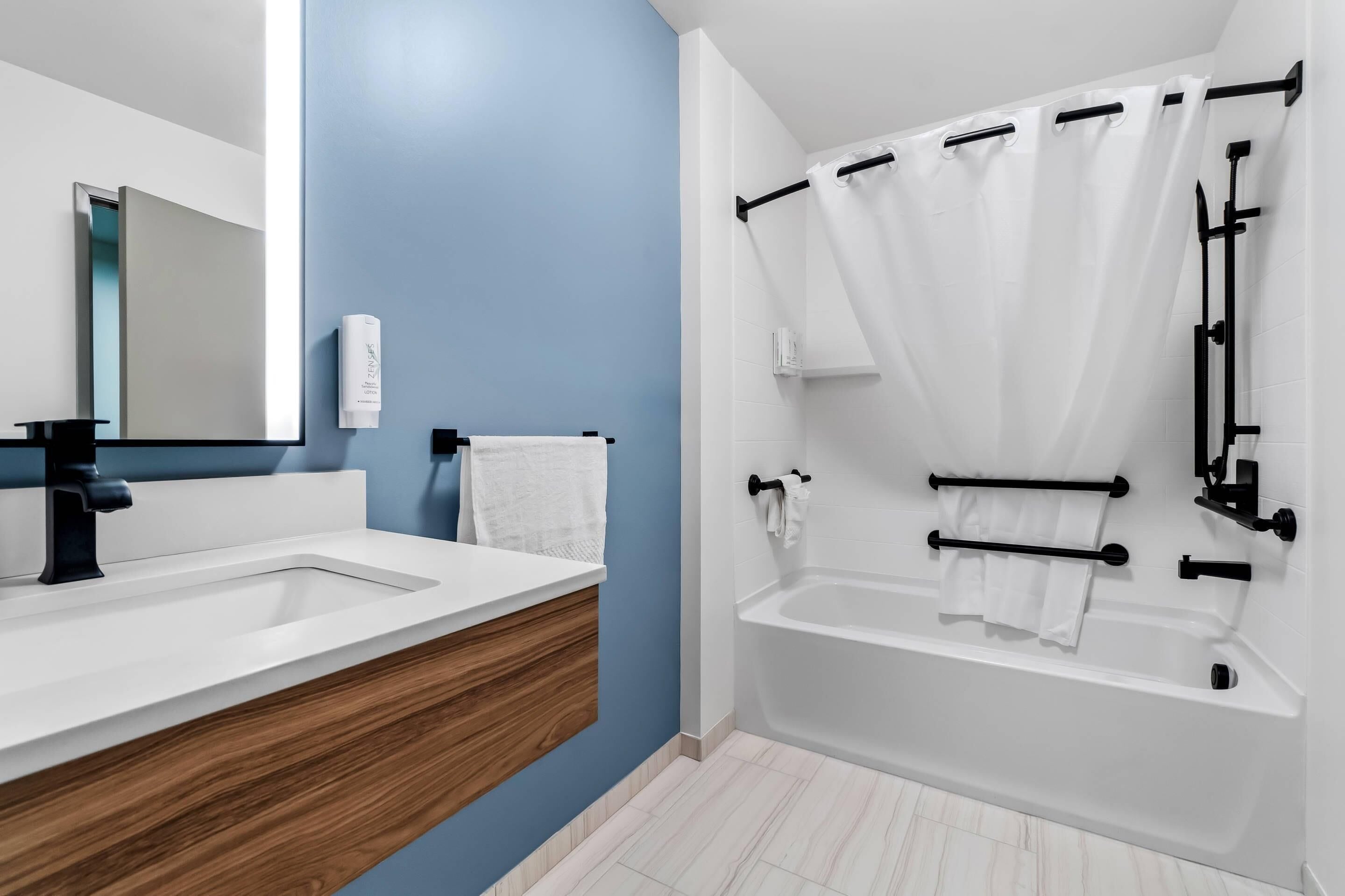 Une salle de bain moderne avec un meuble-lavabo à deux vasques, un grand miroir, une baignoire avec un rideau de douche et un porte-serviettes.