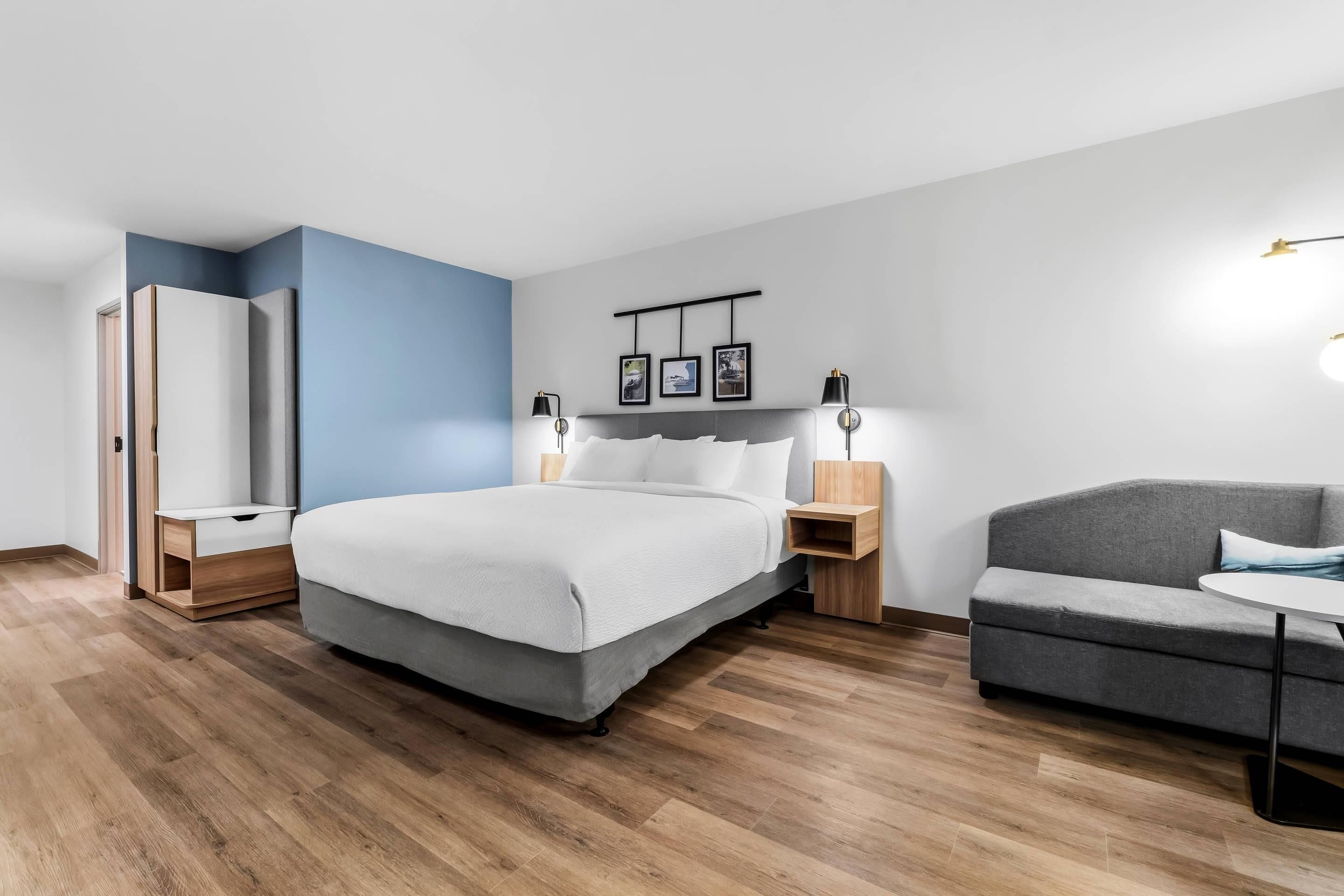Un dormitorio moderno con cama, mesitas de noche, un armario, un sofá y una pequeña mesa.