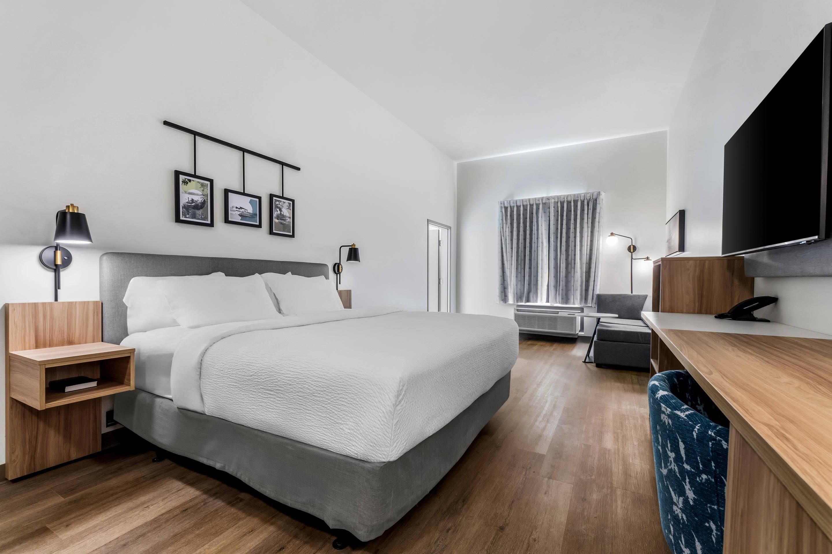 Ein modernes Hotelzimmer mit Bett, Nachttischen, einem Schreibtisch, einem Flachbildfernseher und einem Fenster mit Vorhängen.