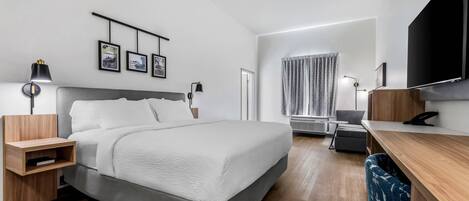 Ein modernes Hotelzimmer mit Bett, Nachttischen, einem Schreibtisch, einem Flachbildfernseher und einem Fenster mit Vorhängen.