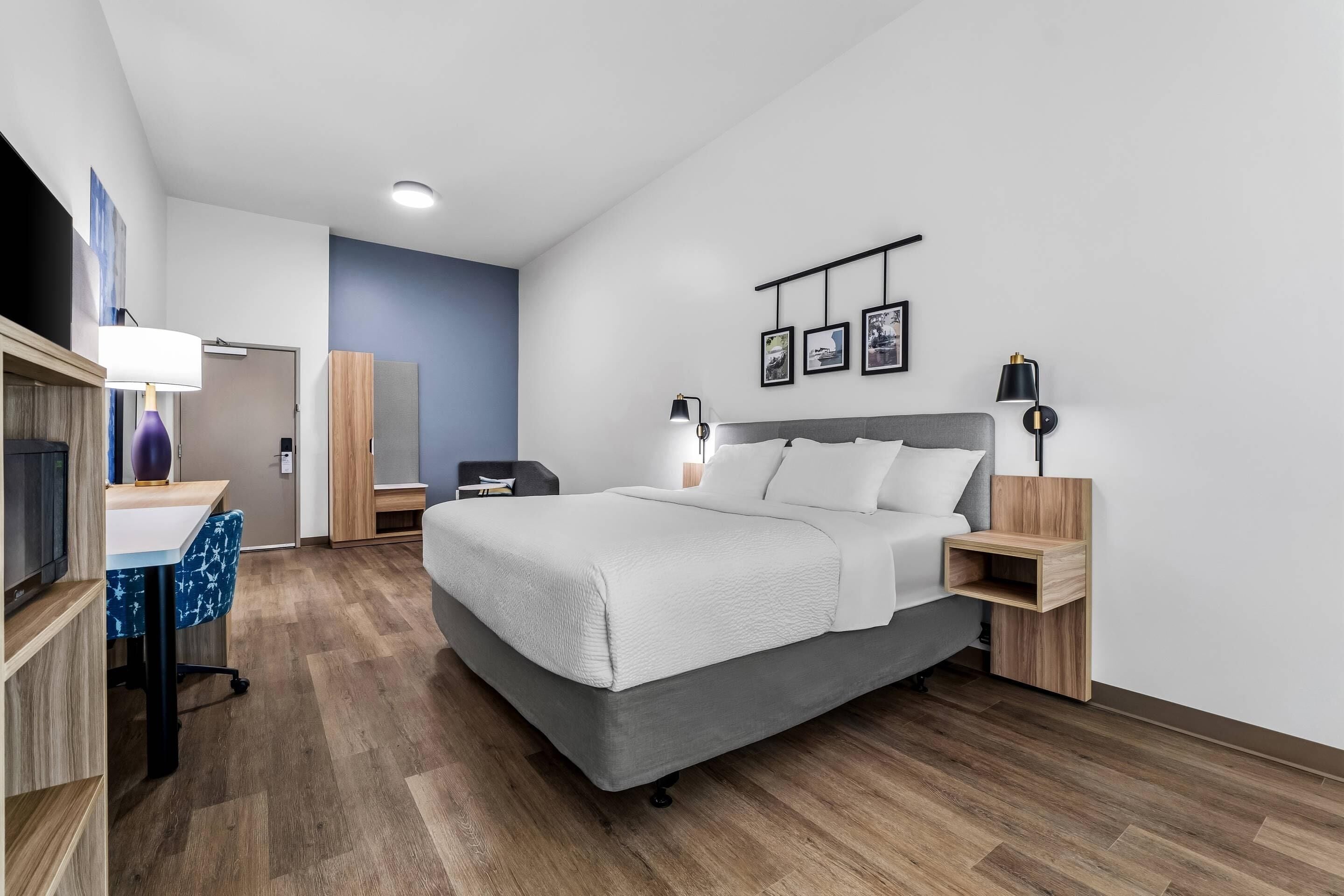 Ein modernes Hotelzimmer mit einem großen Bett, Nachttischen, einem Schreibtisch mit Stuhl, einem Kleiderschrank und einem Fernseher.