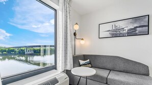 A modern room with a large window, a gray sofa, a small round table, and a framed picture on the wall. - Sleep Inn & Suites Savannah Tennessee Riverfront (Savannah)