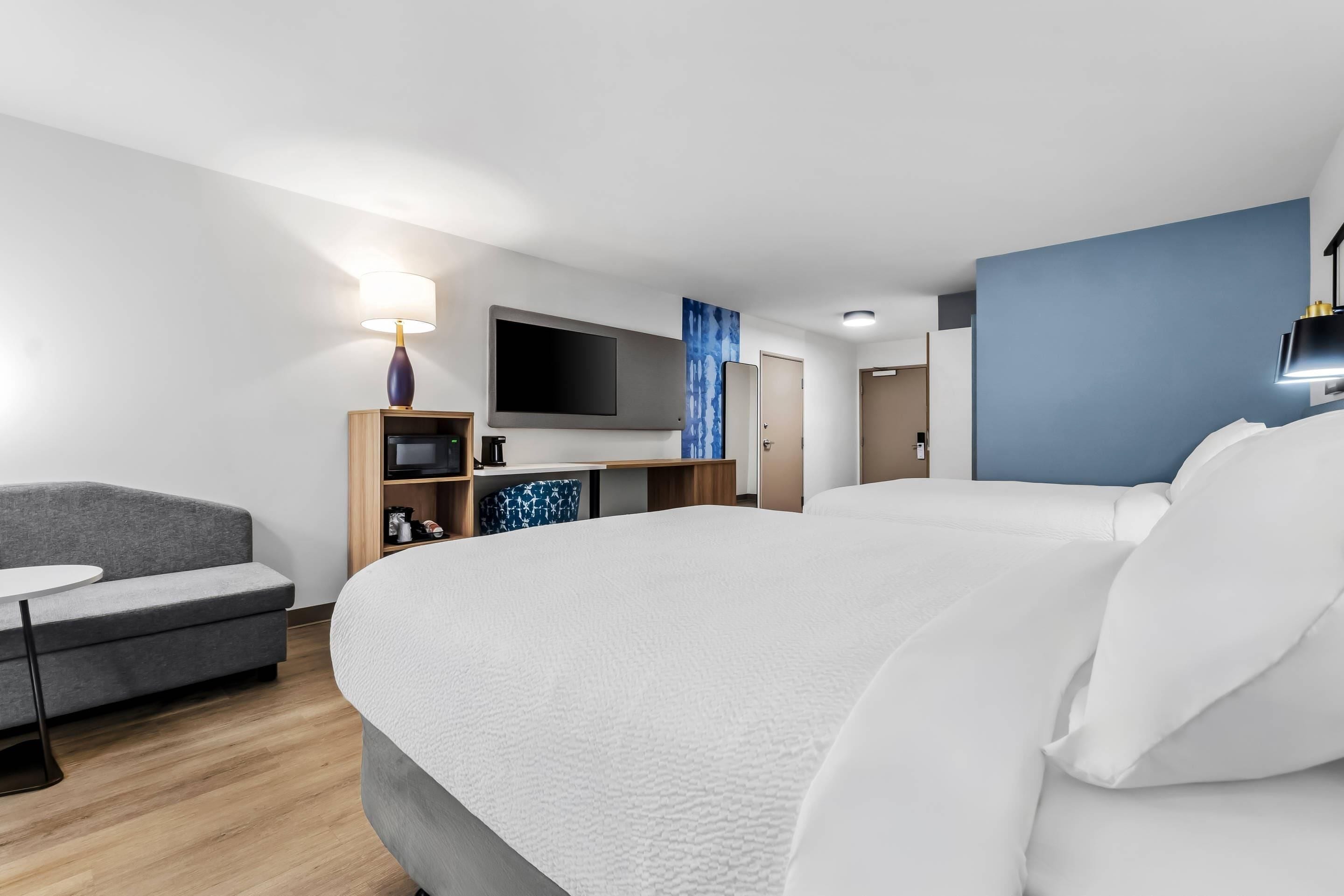 Une chambre d’hôtel avec un lit, un canapé, une télévision, un bureau et un mur d’accent bleu.