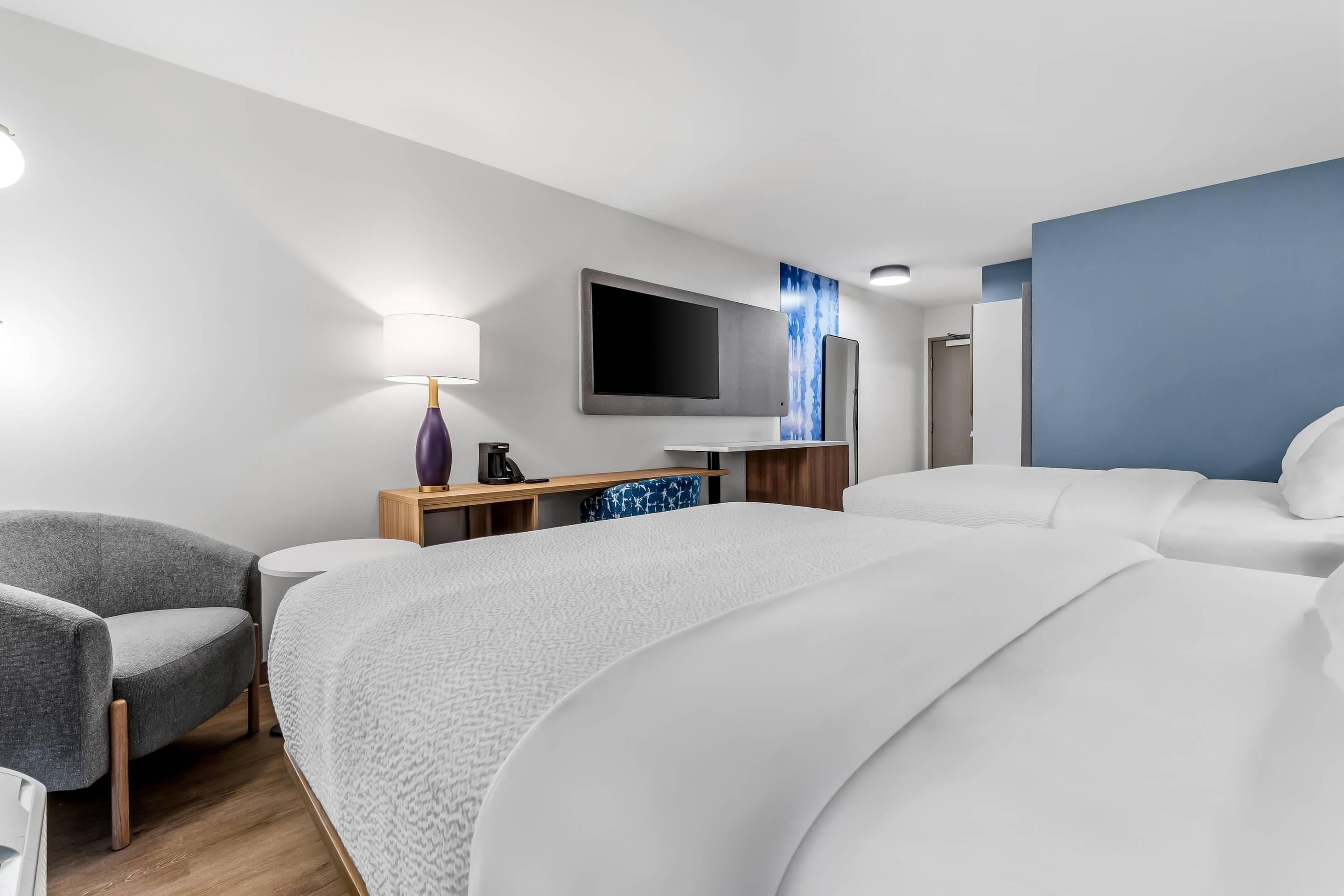 A hotel room with a large bed, a desk with a flat-screen TV, a chair, and a lamp.
