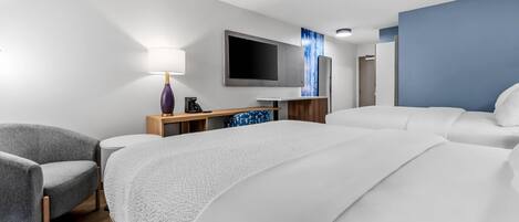 Una habitación de hotel con una cama grande, un escritorio con televisor de pantalla plana, una silla y una lámpara.