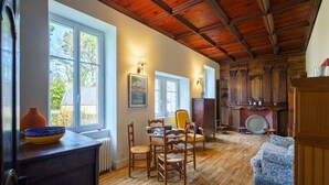 A dining area with wooden flooring, a table with chairs, a vase, and a fireplace with a decorative plate. - Plomarch Pella - à 300m de la plage (Douarnenez)