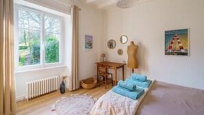 A room with a large window, a wooden desk, a chair, a mannequin, and a bed with blue towels. - Plomarch Pella - à 300m de la plage (Douarnenez)