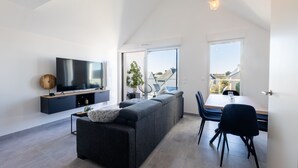 A modern living room with a flat-screen TV, a sofa, a dining table with chairs, and large windows. - L'Escale de Césarine - 1 km de la plage (Carnac)