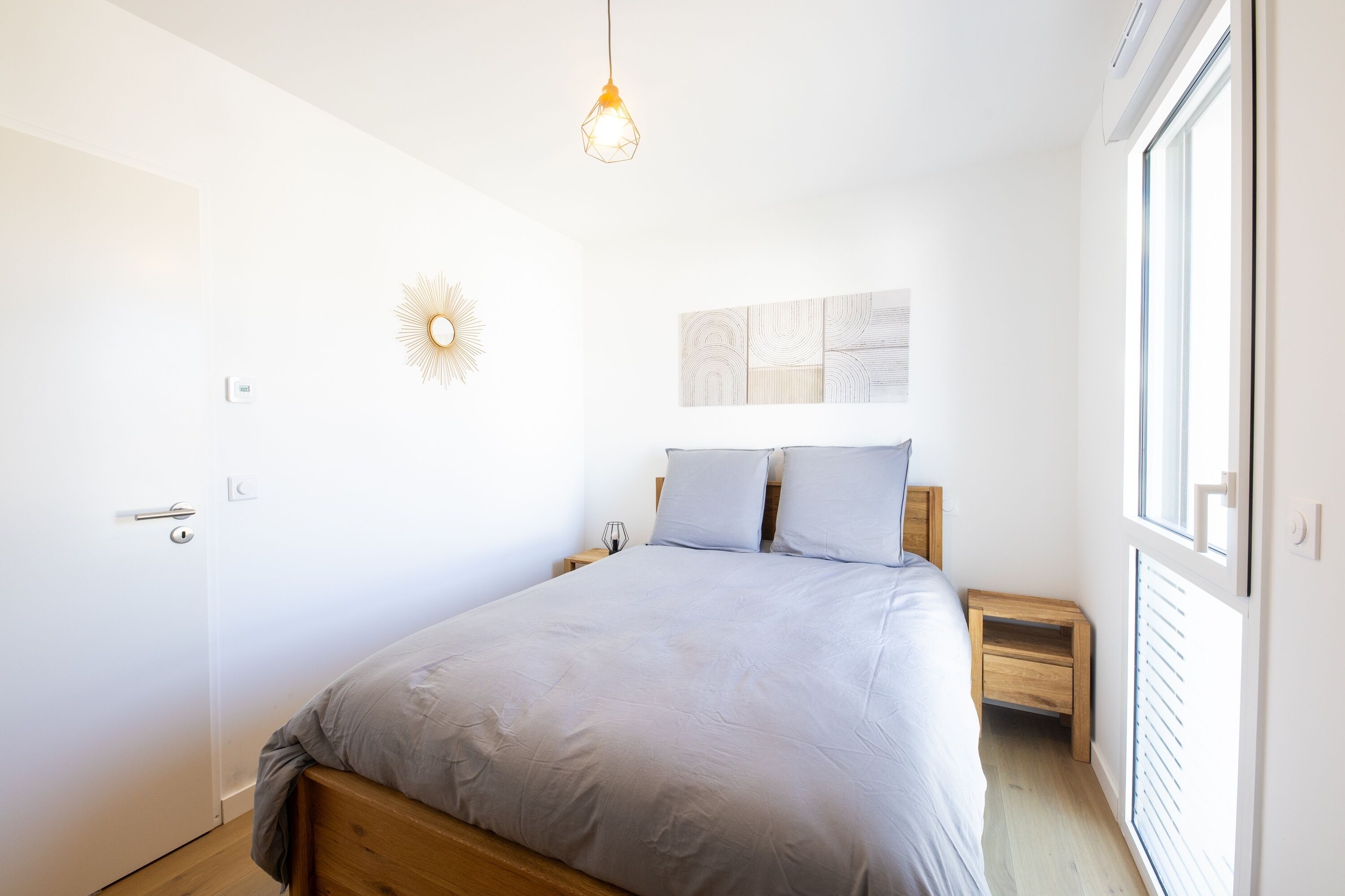 A bedroom with a bed, bedside tables, a wall clock, and a window.