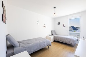 Un dormitorio con dos camas, una mesita de noche, una lámpara colgante, una ventana con vistas y adornos en la pared.