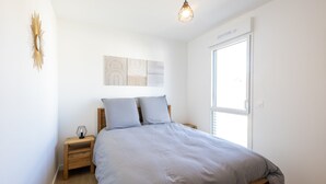A bedroom with a bed, wooden nightstands, a wall art piece, and a window. - L'Escale de Césarine - 1 km de la plage (Carnac)