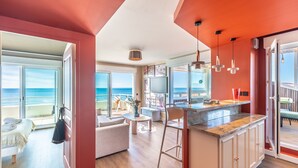 Cozinha moderna com uma ilha grande, área de refeições com vista para a praia e quarto com varanda com vista para o oceano.