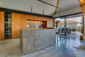 Une cuisine moderne dotée d’un îlot en marbre, de lambris en bois et d’un coin repas avec des chaises.