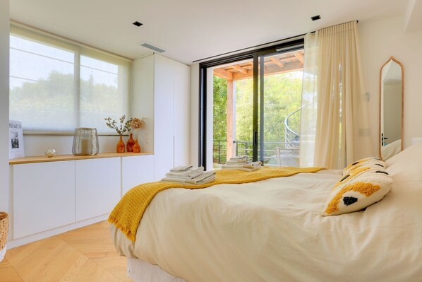 Une chambre à coucher avec un lit, une fenêtre, un miroir et une vue sur la verdure.