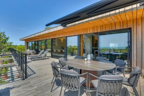 Une terrasse extérieure moderne, dotée d’une table et de chaises, de grandes fenêtres et d’un plafond en bois.