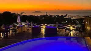 Ein Poolbereich mit Liegestühlen und Sonnenschirmen mit Blick auf einen Sonnenuntergang.