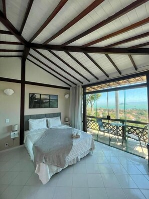 A bedroom with a bed, a nightstand, a wall-mounted lamp, and a large window with a view. - Pousada Bella Vista - Alto da Brava (Buzios)