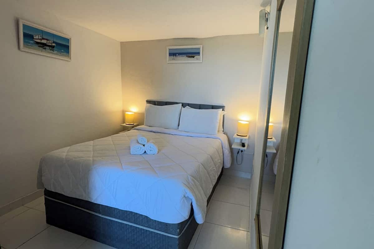 Une chambre à coucher bien rangée, avec un lit, deux lampes de chevet et deux tableaux encadrés accrochés au mur.