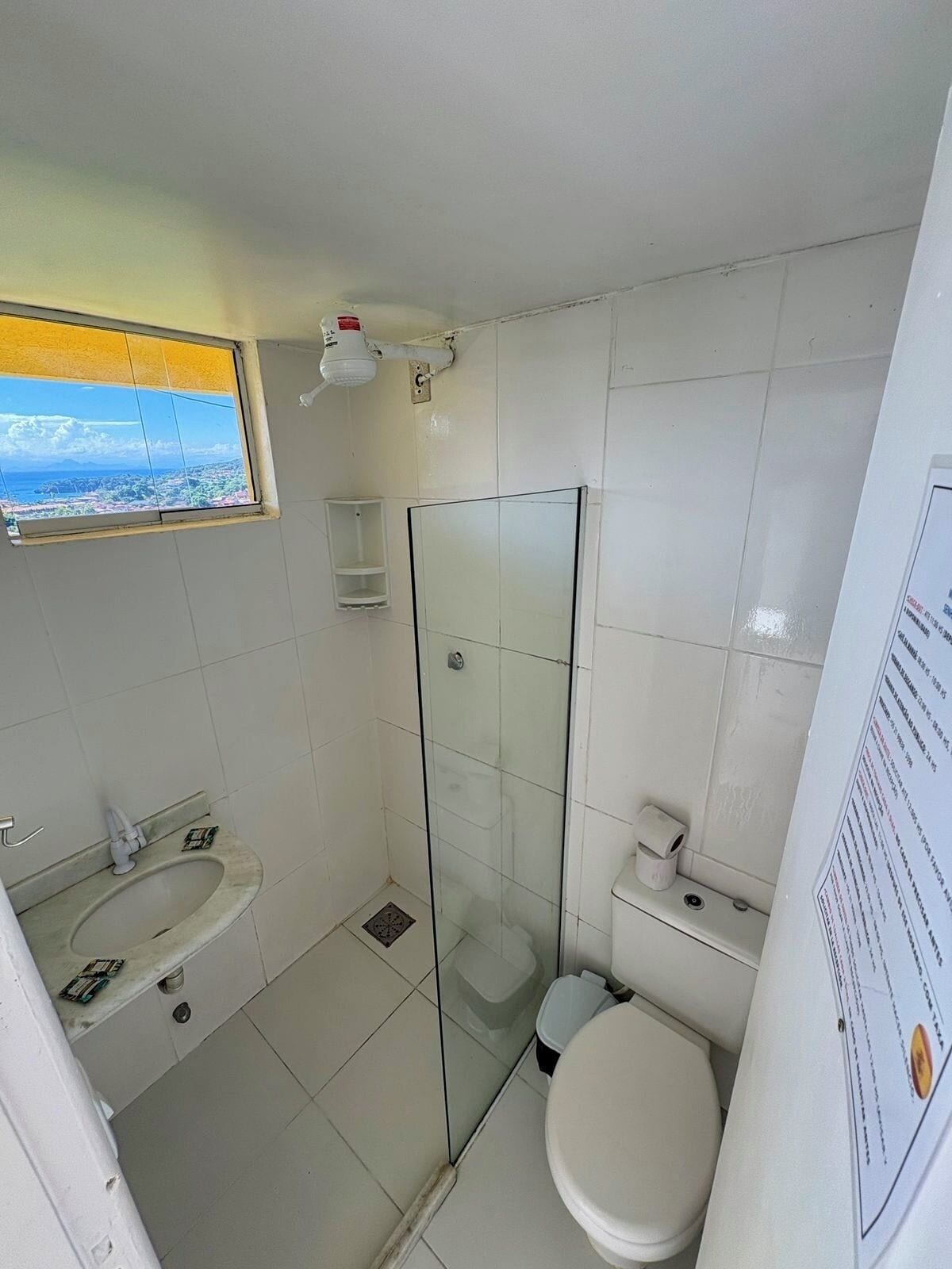 A bathroom with a glass shower enclosure, a toilet, a sink, and a window with a view.
