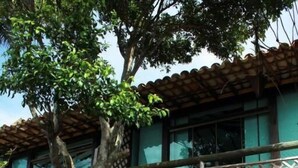 Ein zweistöckiges Gebäude mit Balkon, Steinwänden und einem Baum im Vordergrund.