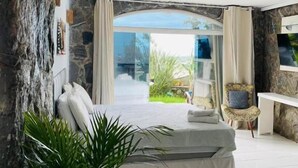 Ein Schlafzimmer mit einer Steinsandsteinwand, einem Bett, einem Sessel und Blick ins Grüne.