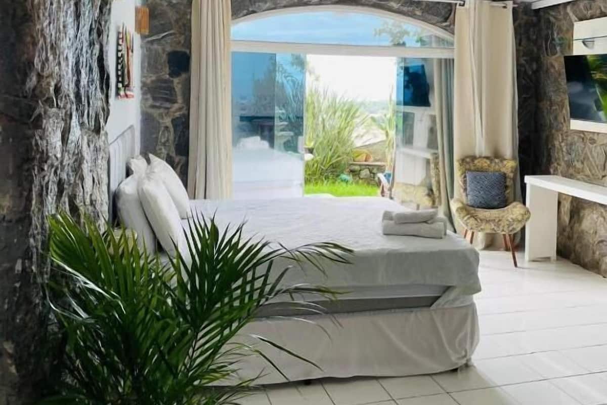 Une chambre avec un mur en pierre, un lit, une chaise et une vue sur la verdure.