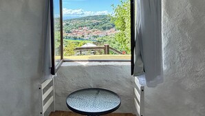 Ein kleines Zimmer mit Fenster, einem runden Tisch und einem Holzsessel.