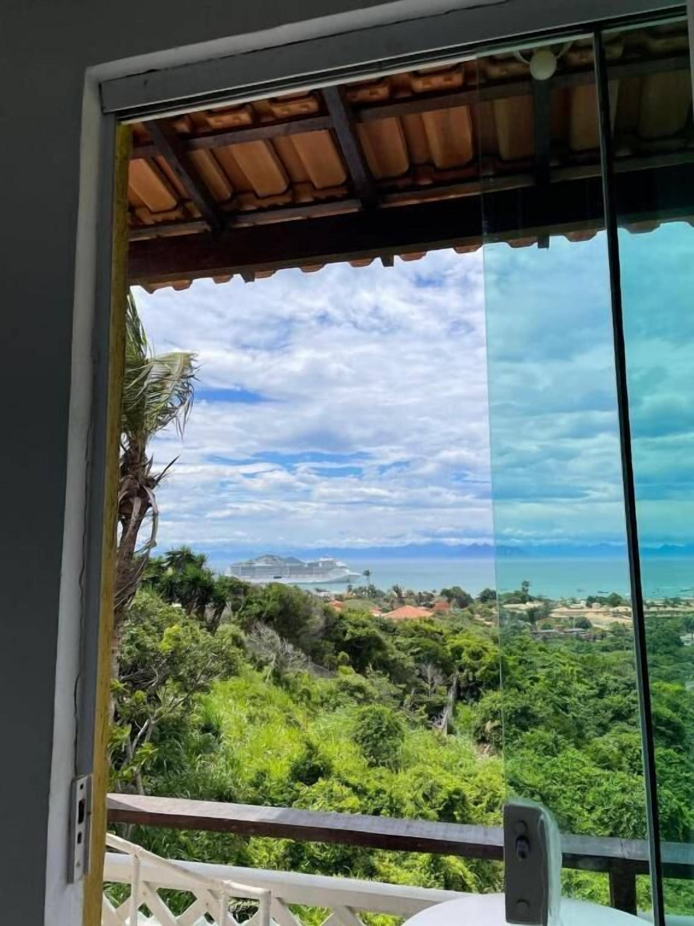 A balcony with a view of a coastal landscape, including a cruise ship and dense greenery.