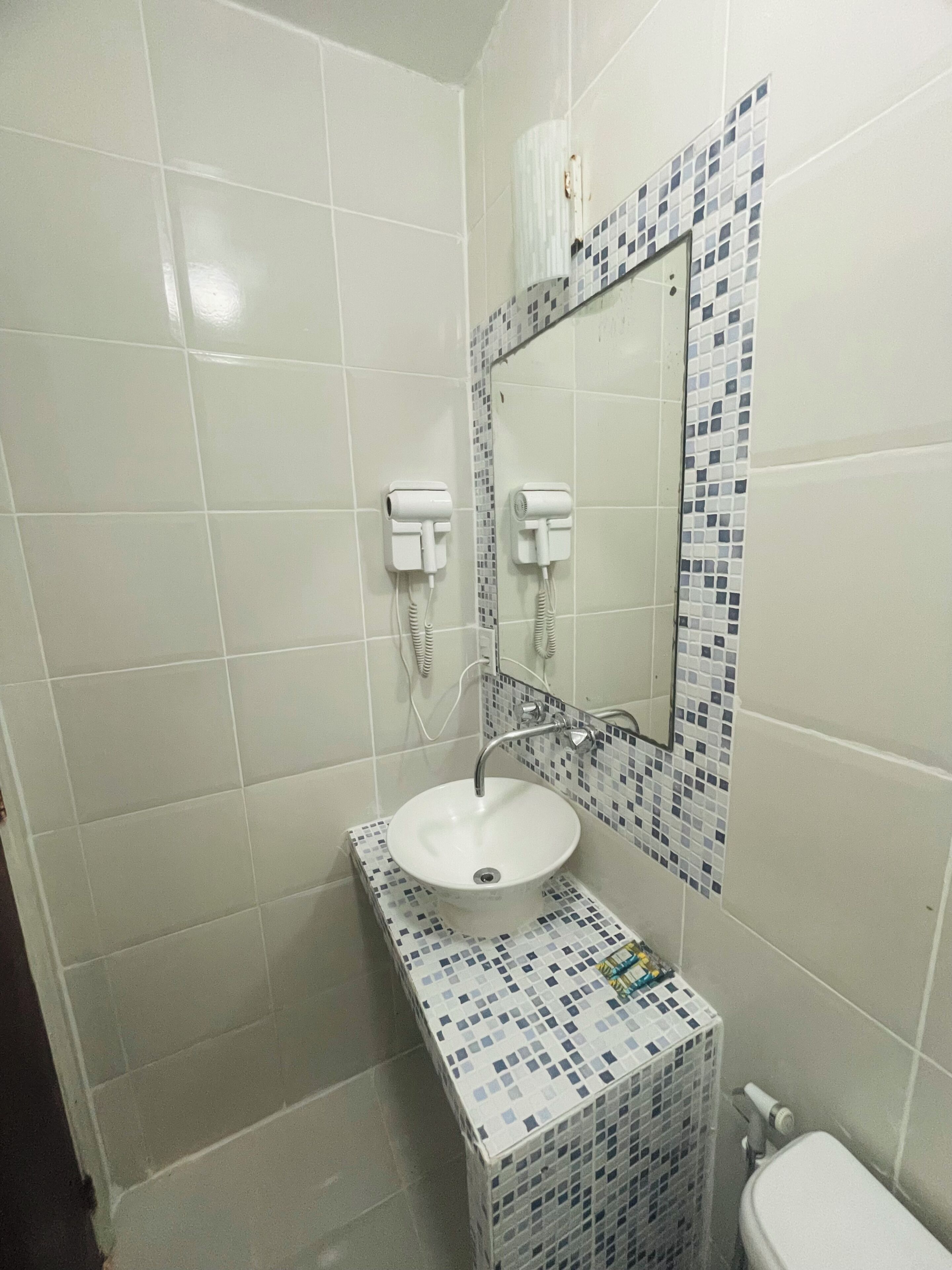 Un baño con un lavamanos blanco, un espejo y una pared con azulejos.