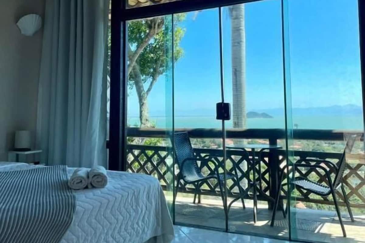 Une chambre d’hôtel avec un lit, une vue sur la mer et un balcon équipé d’une table et de chaises.