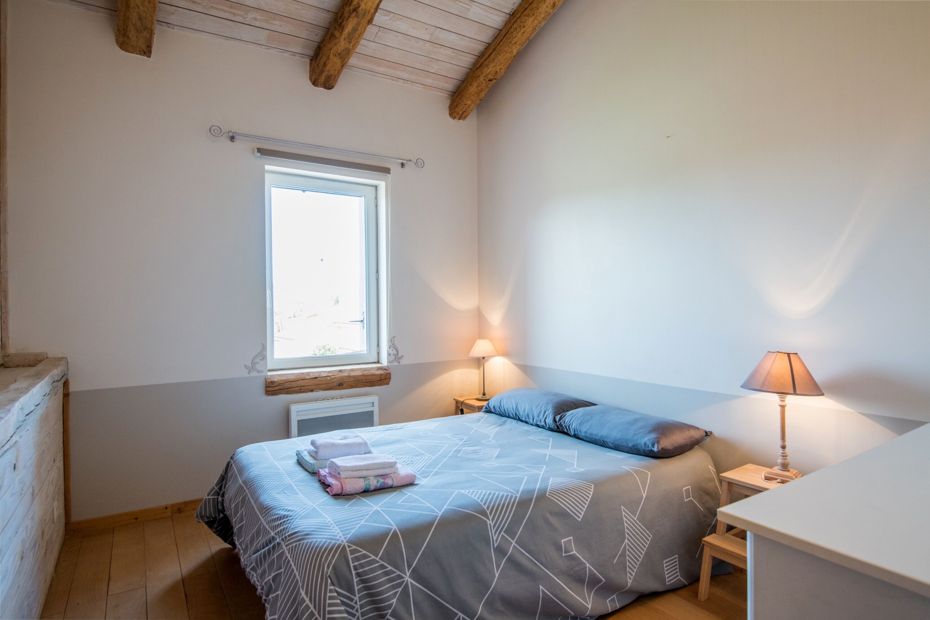Een slaapkamer met een bed, twee bedlampjes, een raam en een houten hoofdeinde.