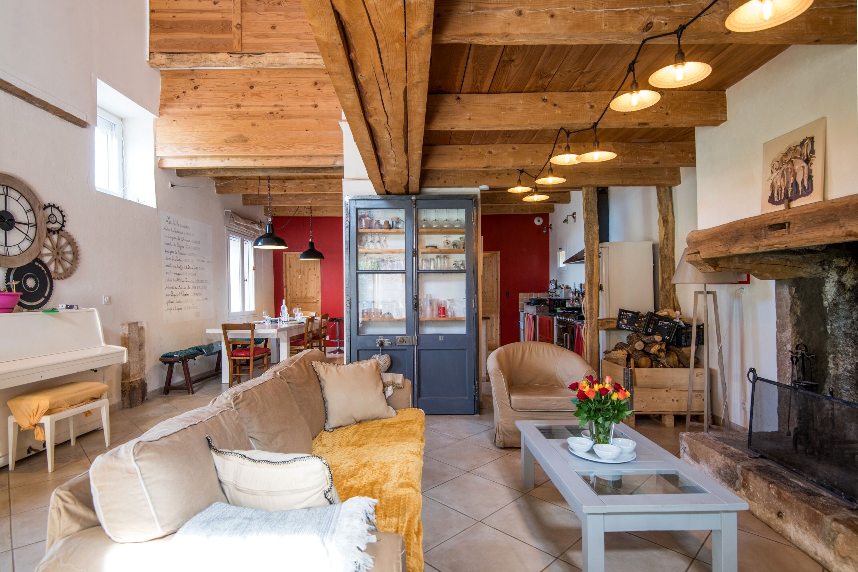 Una sala de estar acogedora con techo de madera, un piano, un sofá, un comedor y una chimenea.