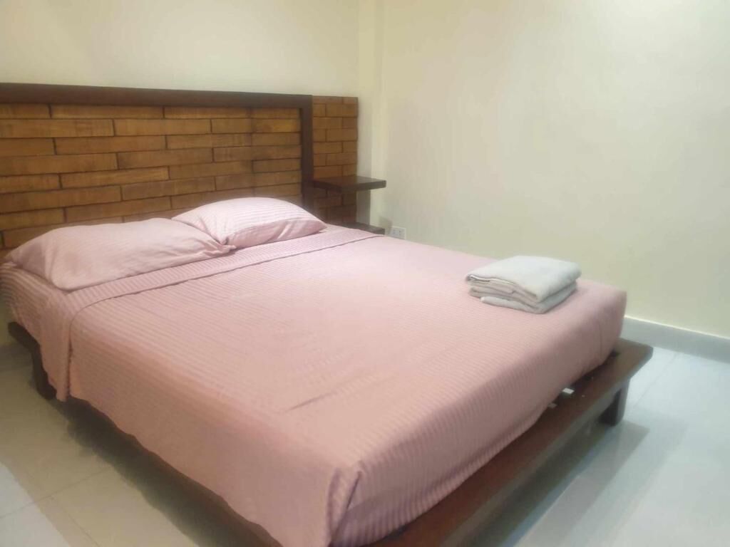 Een eenpersoonsbed met een houten hoofdbord, een roze sprei en een opgevouwen witte handdoek aan het voeteneind.