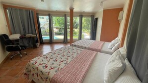 A hotel room with two beds, a desk, a chair, and a view of a swimming pool. - Elicon Suites  (Baclayon)