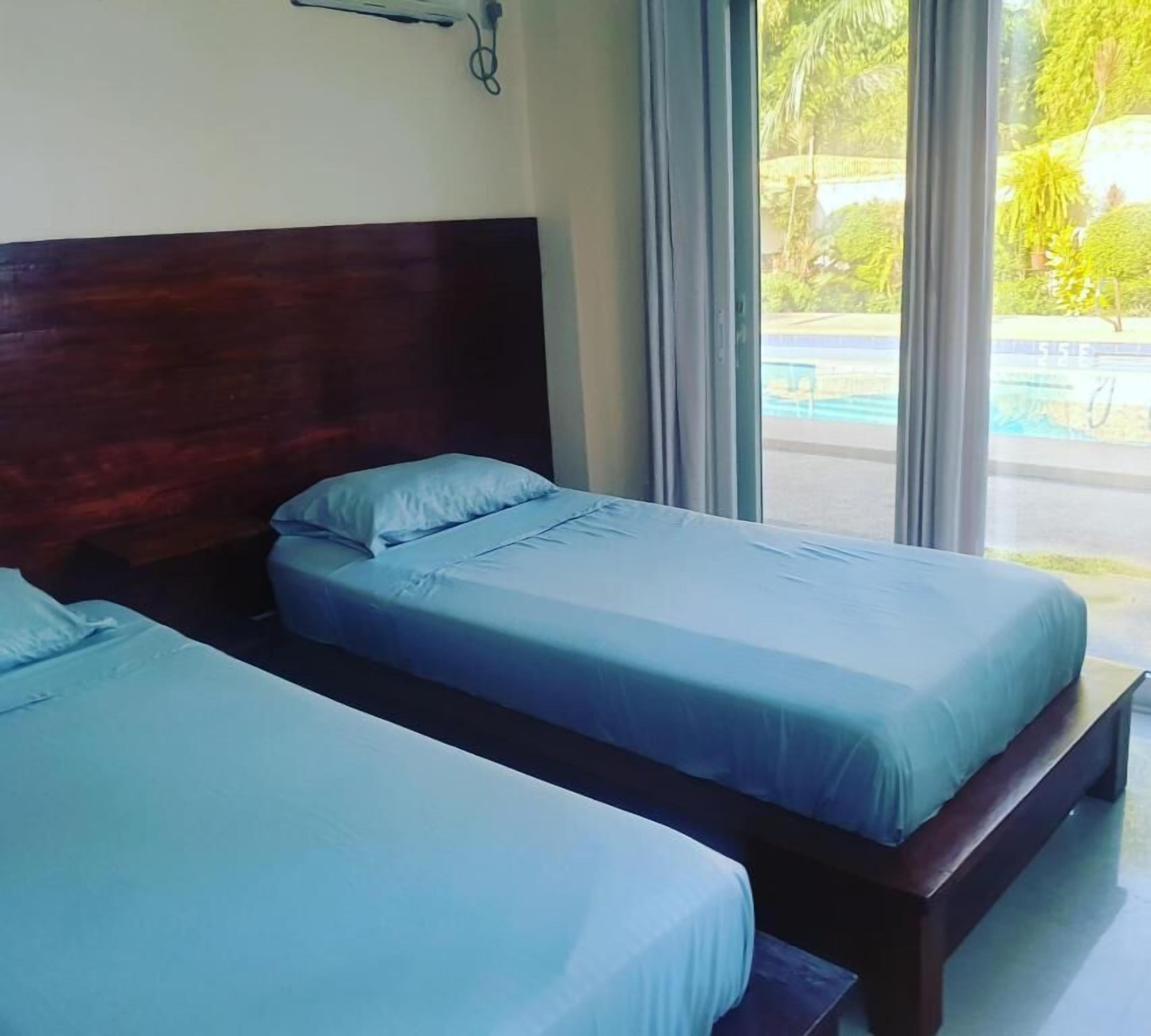 A hotel room with two single beds, a wooden headboard, a window with curtains, and a view of a swimming pool.
