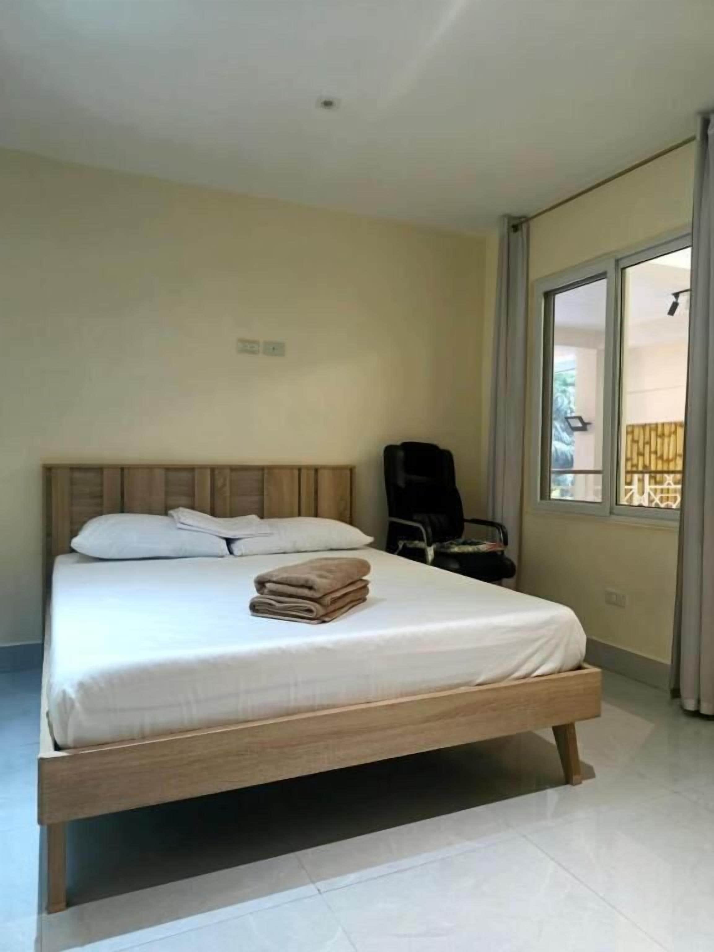 Un dormitorio con cama, almohadas, una toalla doblada, una silla y una ventana.