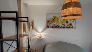 A bedroom with a bed, a bedside table, a lamp, a wall-mounted shelf, and a painting.