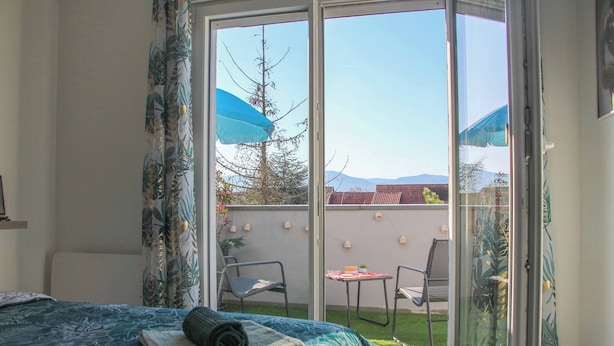 A bedroom with a large sliding glass door leading to a balcony with chairs and a table.