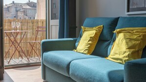 A blue sofa with yellow cushions, a bamboo fence, and a view of buildings through a window.